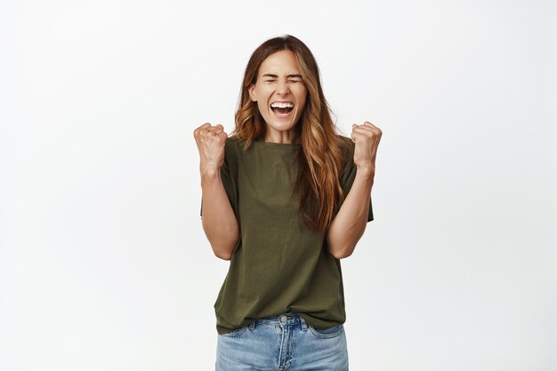 Ambiciosa mujer exitosa, ganadora de mediana edad, grita de alegría y deleite, aprieta el puño como ganadora, se convierte en campeona, logra la meta, celebra la victoria, fondo blanco.