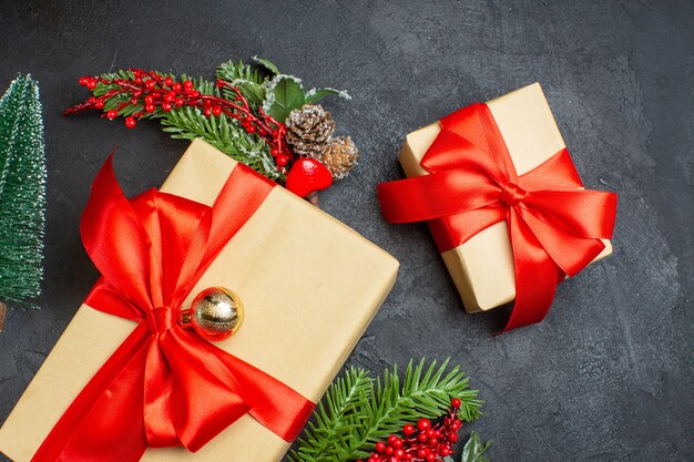 Ambiente navideño con hermosos regalos con cinta en forma de lazo y accesorios de decoración de ramas de abeto sobre un fondo oscuro