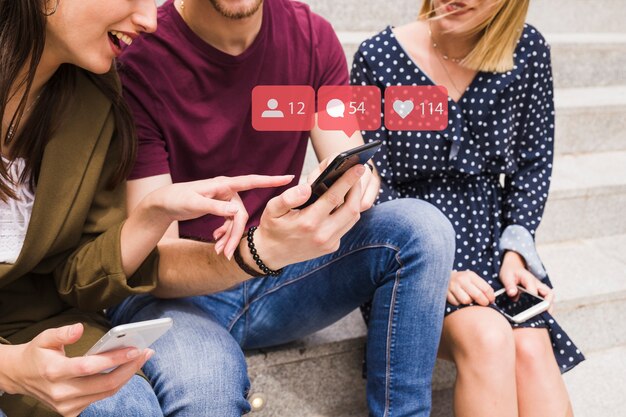Una amiga apuntando al hombre usando iconos de notificación de red social sobre el móvil