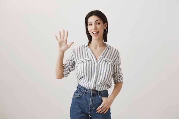 Amigable chica atractiva agitando la mano para saludar, saludando a los invitados