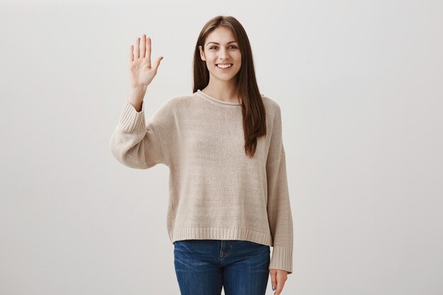 Amigable chica caucásica diciendo hola, agitando la mano en gesto de saludo, saludando a amigos