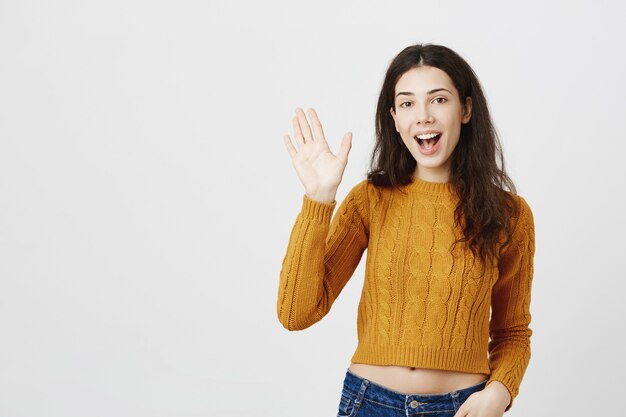 Amigable chica morena diciendo hola, saludando con la mano en señal de saludo, gusto en conocerte gesto