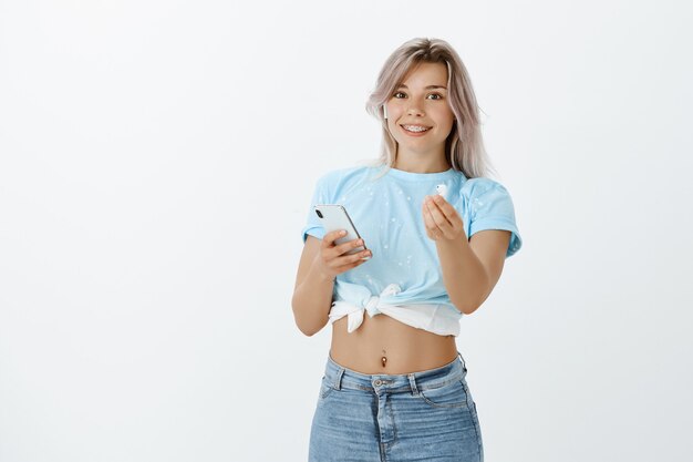 Amigable chica rubia posando en el estudio con su teléfono y auriculares