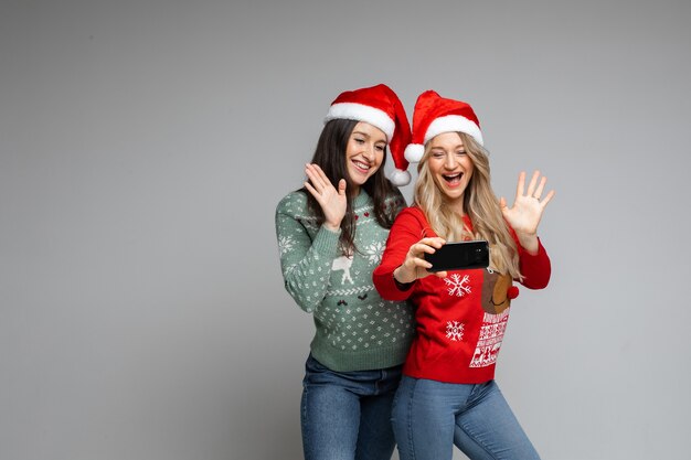 Amigas atractivas con sombreros navideños rojos y blancos hacen selfie con un teléfono