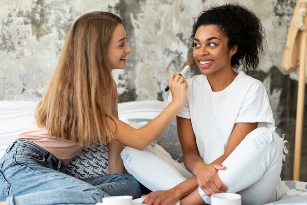 Amigas ayudándose unos a otros con maquillaje en la cama