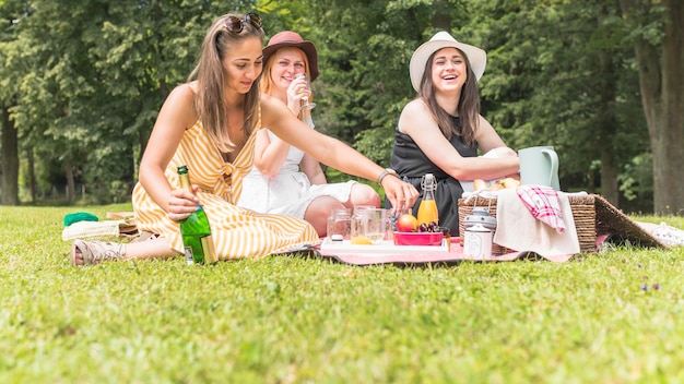 Amigas disfrutando de bebidas y frutas en picnic