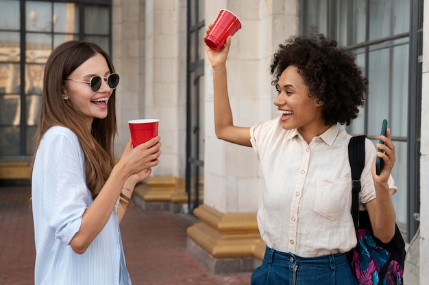 Foto gratuita amigas divirtiéndose juntos al aire libre con vasos de plástico