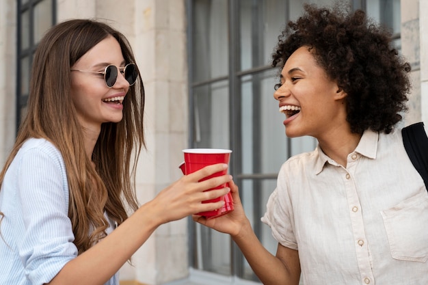 Amigas divirtiéndose juntos al aire libre con vasos de plástico