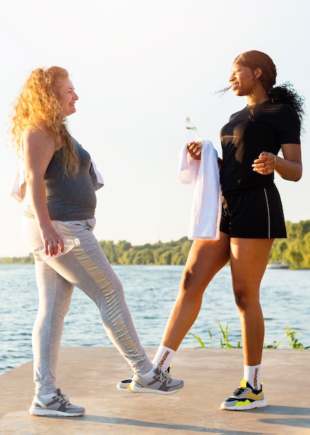 Amigas haciendo el saludo de tobillo mientras hace ejercicio junto al lago