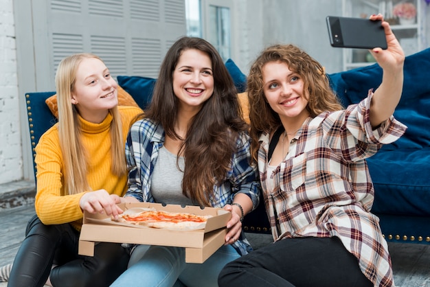 Amigas haciéndose un selfie comiendo pizza