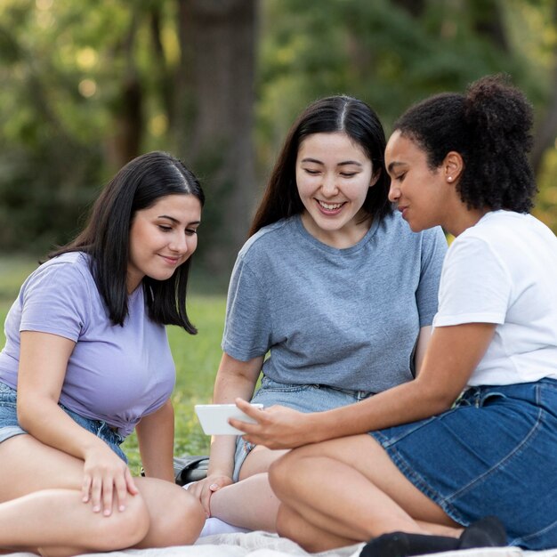 Amigas juntas en el parque con smartphone