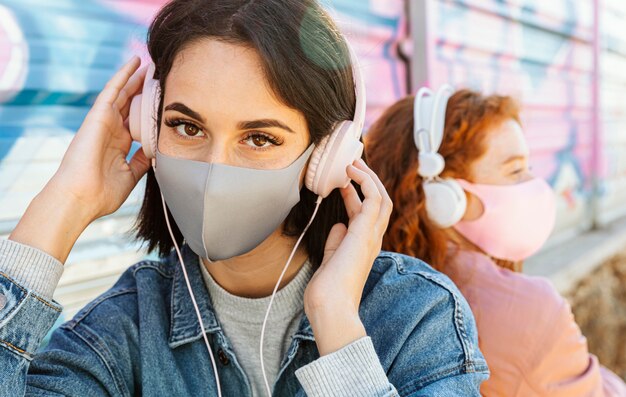 Amigas con máscaras faciales al aire libre escuchando música con auriculares