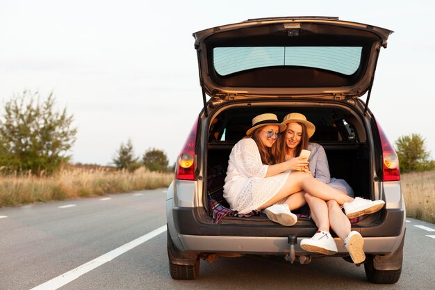 Amigas mirando smartphone mientras está en el maletero del coche