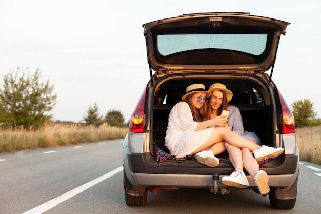 Foto gratuita amigas mirando smartphone mientras está en el maletero del coche