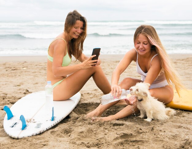 Amigas en la playa con perro y smartphone