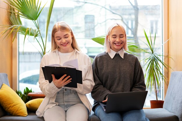 Amigas que estudian en una biblioteca mientras usan una computadora portátil y una libreta