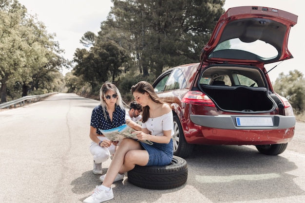 Amigas que miran el mapa que se sienta cerca del coche analizado en el camino