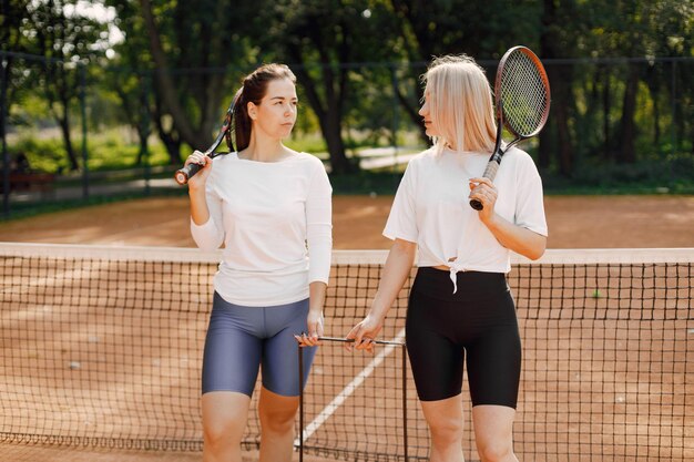 Amigas con raquetas y caja de pelotas en la cancha de tenis. Verano, fuera de la cancha.