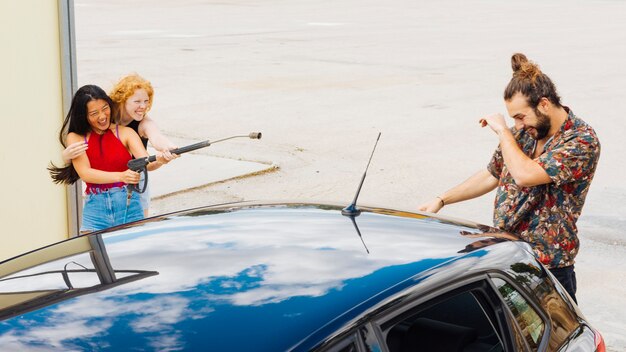 Amigas salpicando agua en hombre detrás de coche