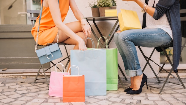 Amigas sentadas en cafetería con bolsas de compra