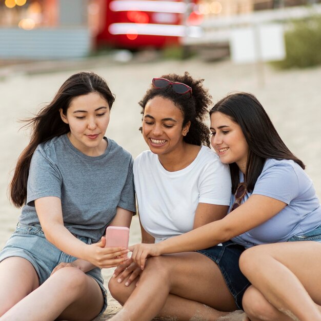 Amigas sentadas en la playa con smartphone