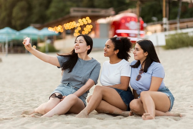 Amigas sentadas en la playa y tomando selfie