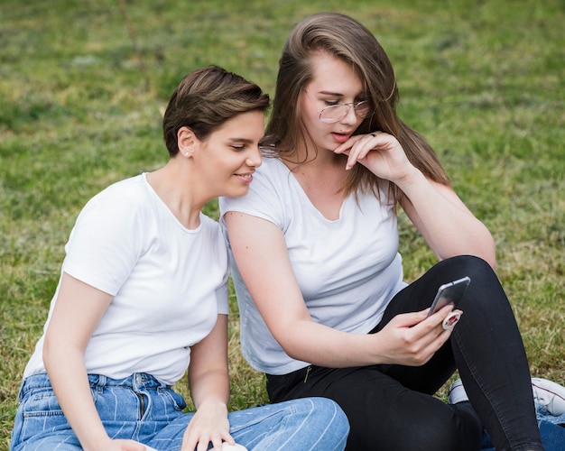 Amigas con smartphone sentado en el césped