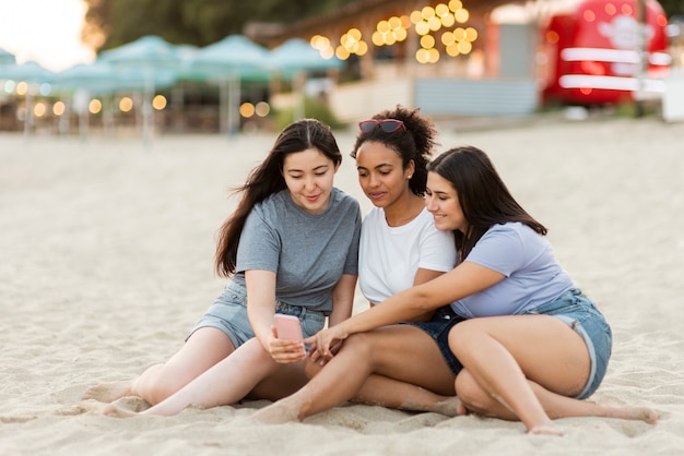 Amigas con smartphone sentado en la playa