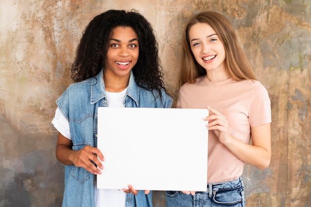 Amigas sonrientes con cartel en blanco