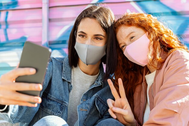 Amigas sonrientes con máscaras faciales al aire libre tomando un selfie