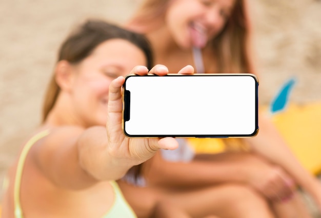 Amigas sonrientes en la playa con smartphone