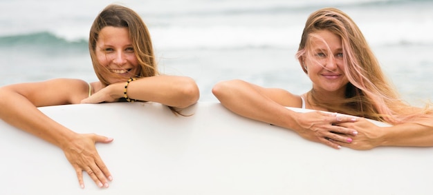 Amigas sonrientes en la playa con tabla de surf