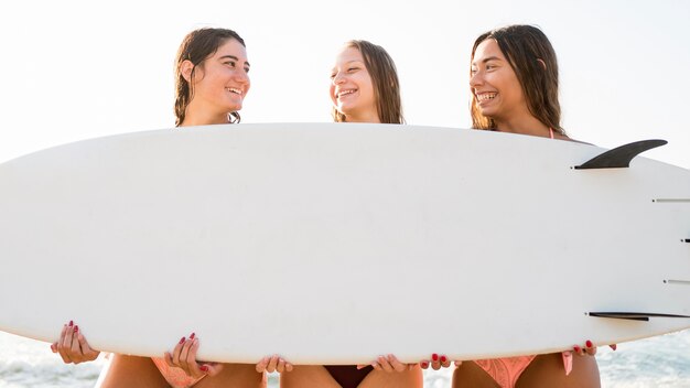 Amigas de tiro medio sosteniendo la tabla de surf