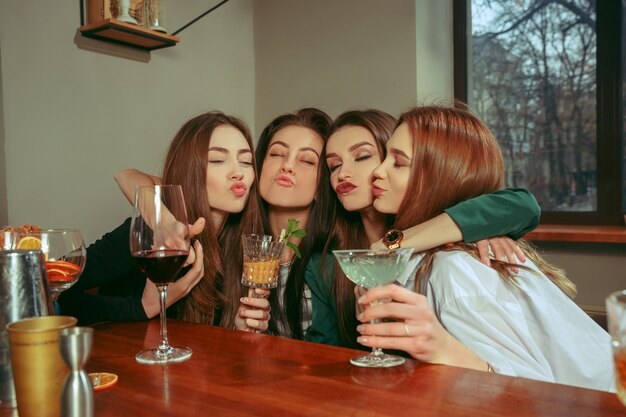 Amigas tomando una copa en el bar. Están sentados en una mesa de madera con cócteles. Llevan ropa informal.