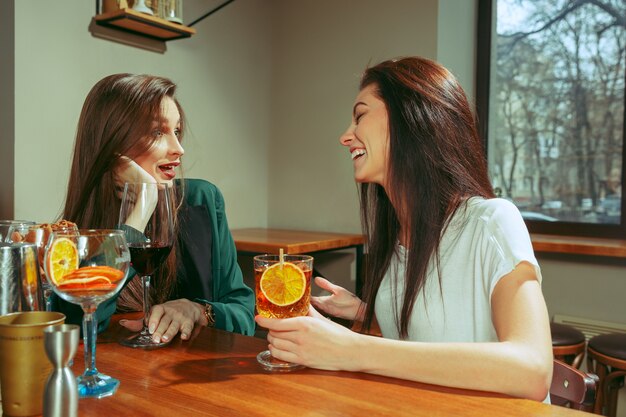 Amigas tomando una copa en el bar. Están sentados en una mesa de madera con cócteles.