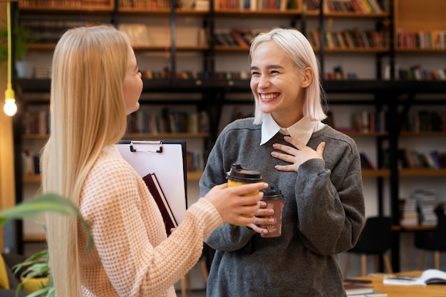 Amigas tomando libros de una biblioteca y bebiendo café