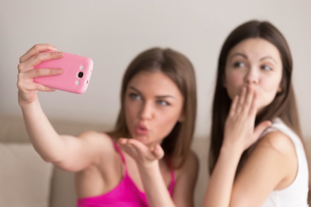 Amigas tomando selfie y enviando besos de aire.