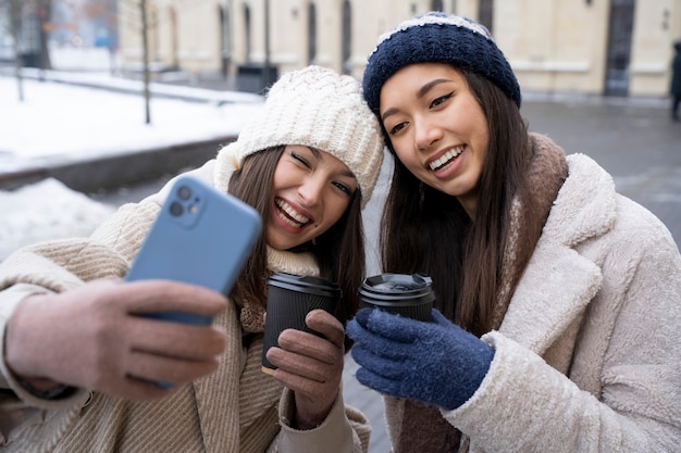 Amigas tomándose una selfie y sosteniendo tazas de café al aire libre después de reunirse