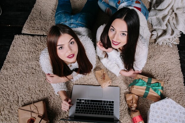 Amigas tumbadas en el suelo con un portátil y mirando hacia arriba