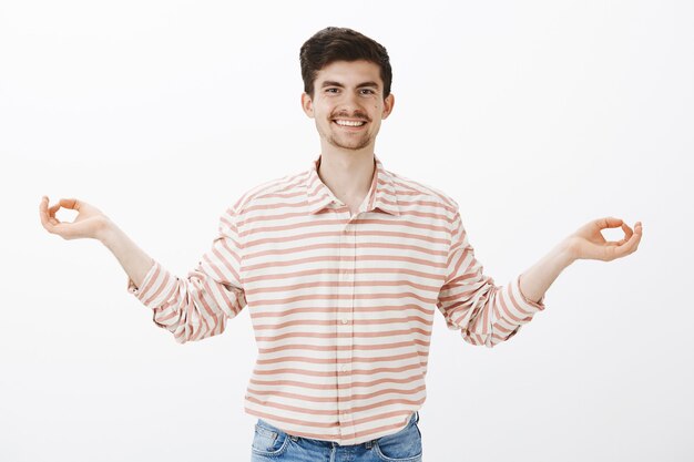 Amigo alegre que muestra cómo empezar a meditar. Retrato de hombre atractivo de aspecto amable positivo con bigote y barba, extendiendo las manos en gesto zen y sonriendo ampliamente, practicando yoga