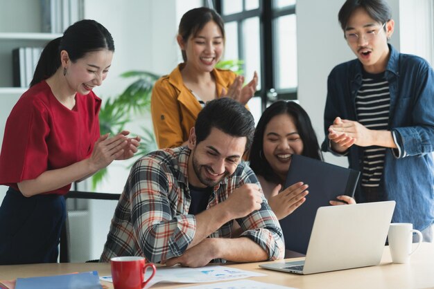 Amigo creativo asiático hipster de moda sonriendo mientras se sienta en una reunión informal con un grupo de amigos, un compañero de trabajo está trabajando en un nuevo proyecto de éxito mientras usa computadoras portátiles digitales