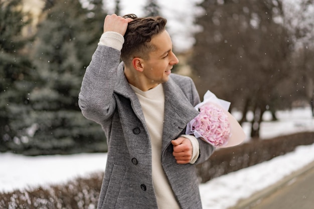 Amigo con un ramo de hortensias de flores rosas esperando a su novia al aire libre mientras cae la nieve. Concepto del día de Valetnine, propuesta de boda. el hombre va a una cita.