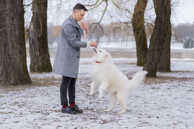 Amigo con un ramo de hortensias de flores rosas esperando a su novia y caminando y jugando con un perro. al aire libre mientras cae la nieve. Concepto del día de Valetnine, propuesta de boda. mangos