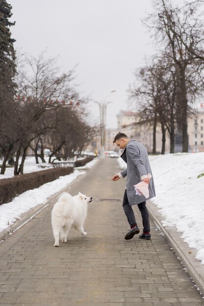 Amigo con un ramo de hortensias de flores rosas esperando a su novia y caminando y jugando con un perro. al aire libre mientras cae la nieve. Concepto del día de Valetnine, propuesta de boda. mangos