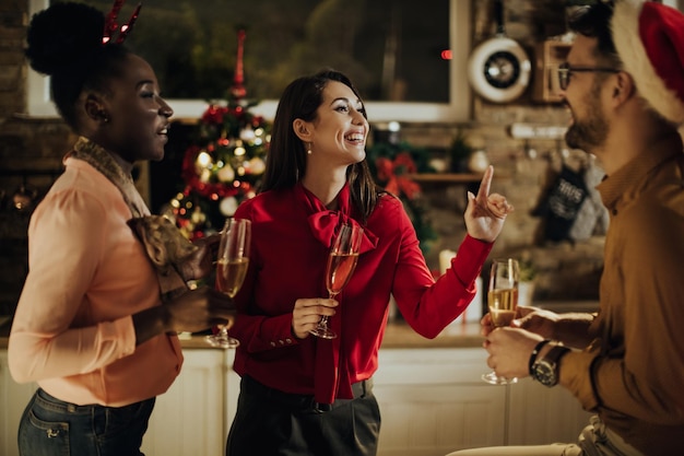 Amigos alegres divirtiéndose mientras beben champán y hablan en la víspera de Año Nuevo en casa