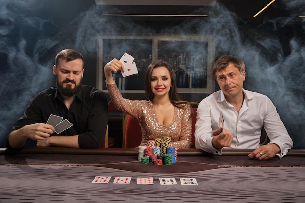 Foto gratuita amigos alegres están jugando al póquer en el casino en humo. la chica ha ganado y mostrando sus cartas, los hombres han perdido. los jóvenes están haciendo apuestas esperando una gran victoria. juegos de azar por dinero. juegos de fortuna.