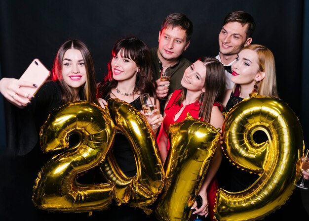 Amigos alegres haciendo selfie con globos numero 2019