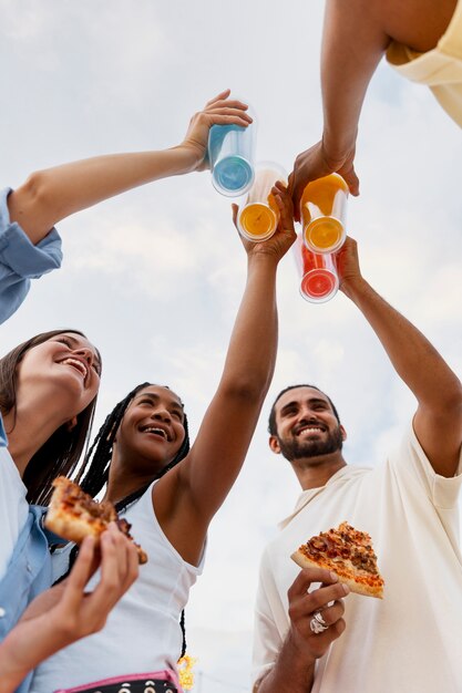 Amigos de ángulo bajo con pizza y bebidas.