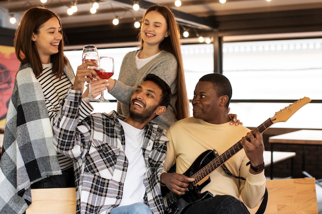 Amigos animando copas de vino mientras escuchan a su amigo tocando la guitarra