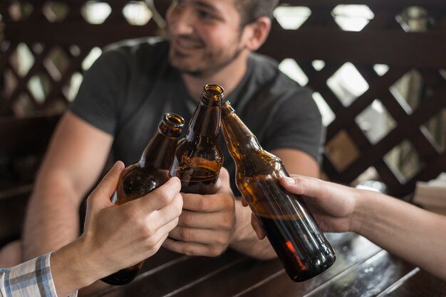 Amigos anónimos que tintinean botellas y mesa de bar